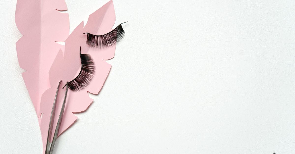 Black false lashes strips with tweezers on pink paper leaves